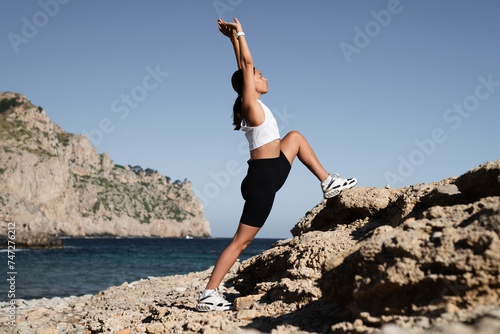 Caucasian young fit athlete female sportswoman stretching, warming up before training, working out in fitness yoga clothes by the beach outdoors. Healthy lifestyle concept