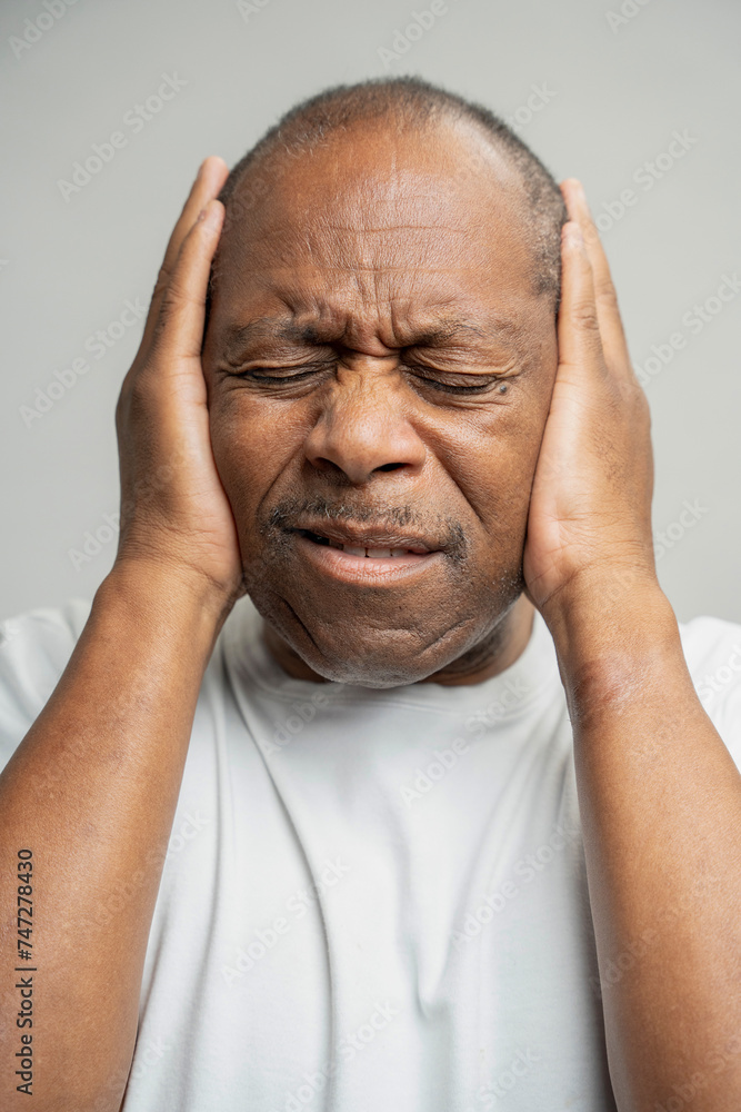 Portrait of man covering ears with hands against gray background Portrait of man covering ears with hands against gray background