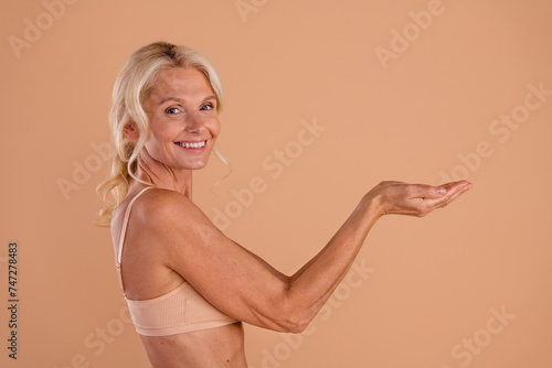 Photo of adorable sweet middle age woman wear bikini showing arms empty space smiling isolated beige color background