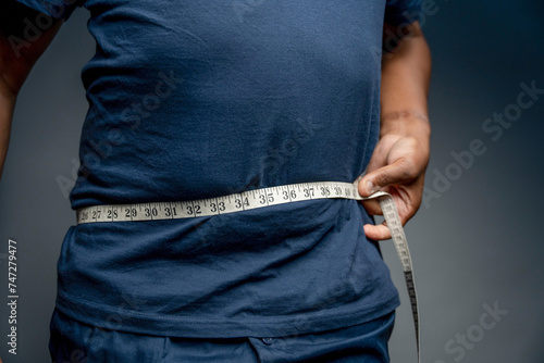 Fotografi Senior man measuring waist against gray background