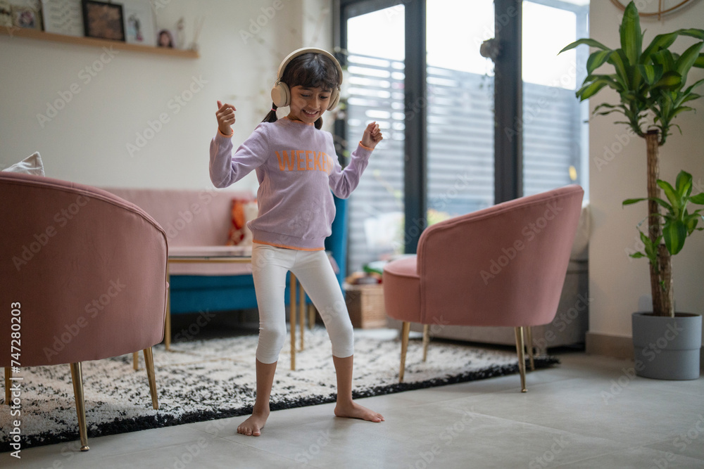 Little girl dancing with headphones in living room - obrazy, fototapety, plakaty 