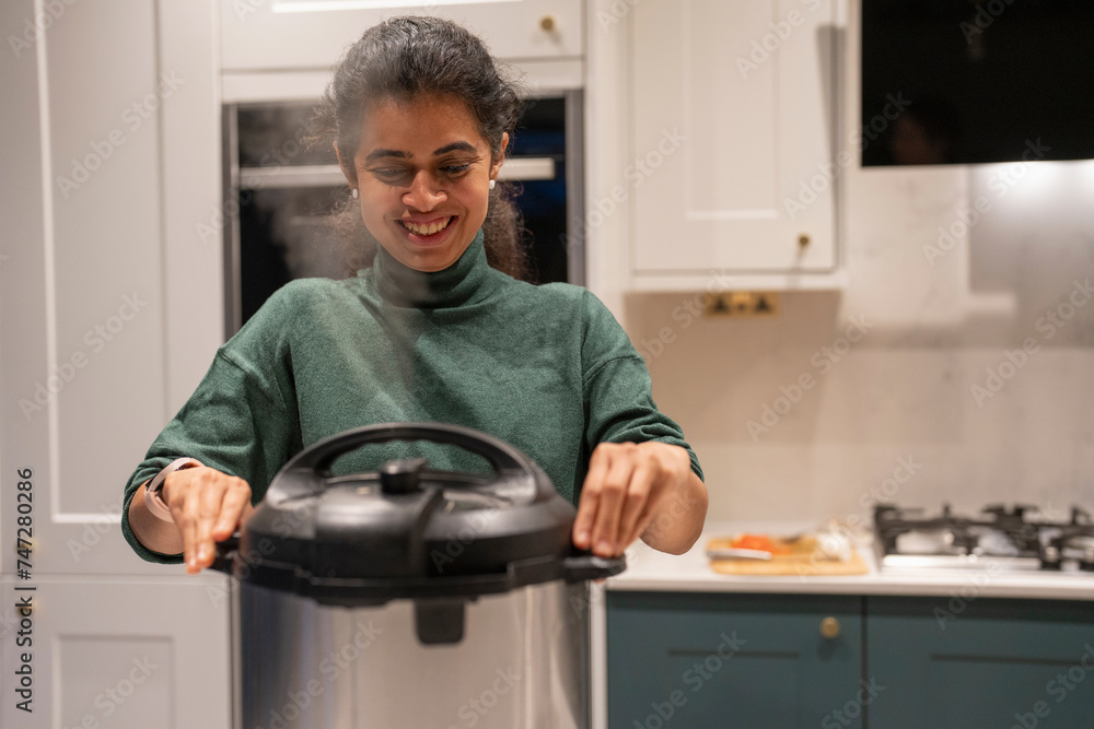 Woman opening pressure cooker pot in kitchen - obrazy, fototapety, plakaty 