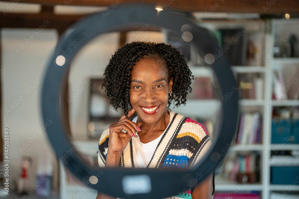 Portrait of smiling woman standing in front of ring light at home - obrazy, fototapety, plakaty 