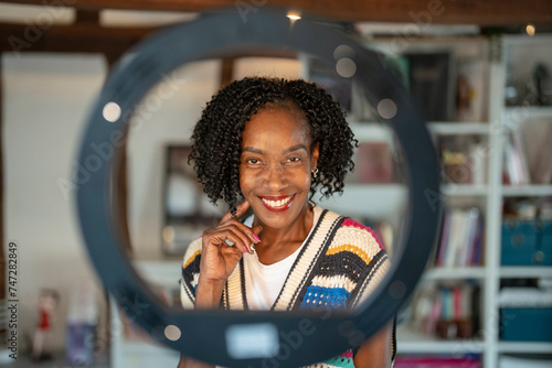 Portrait of smiling woman standing in front of ring light at home photo