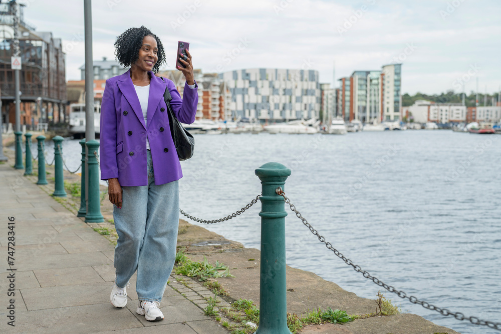 Smiling woman photographing city view with smart phone during walk