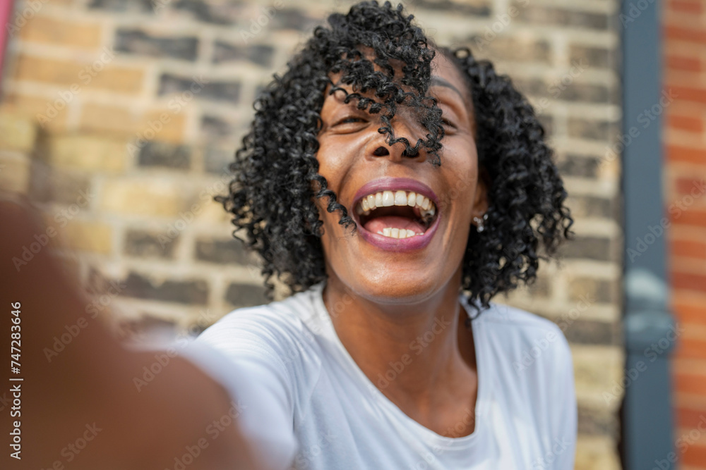 Portrait of woman laughing while taking selfie against brick wall Portrait of woman laughing while taking selfie against brick wall