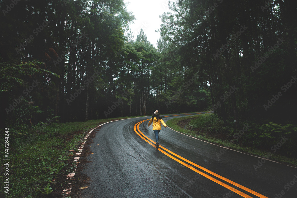 Obraz premium Woman in yellow raincoat running on road in pine forest