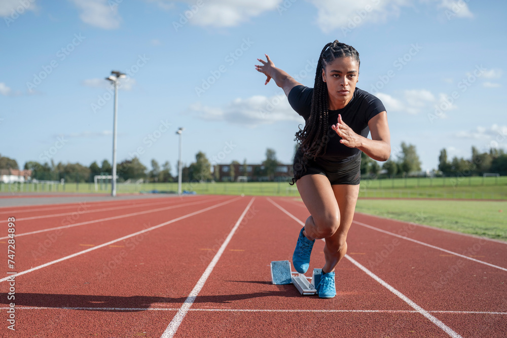 Fototapeta premium Female athlete sprinting off starting line at stadium
