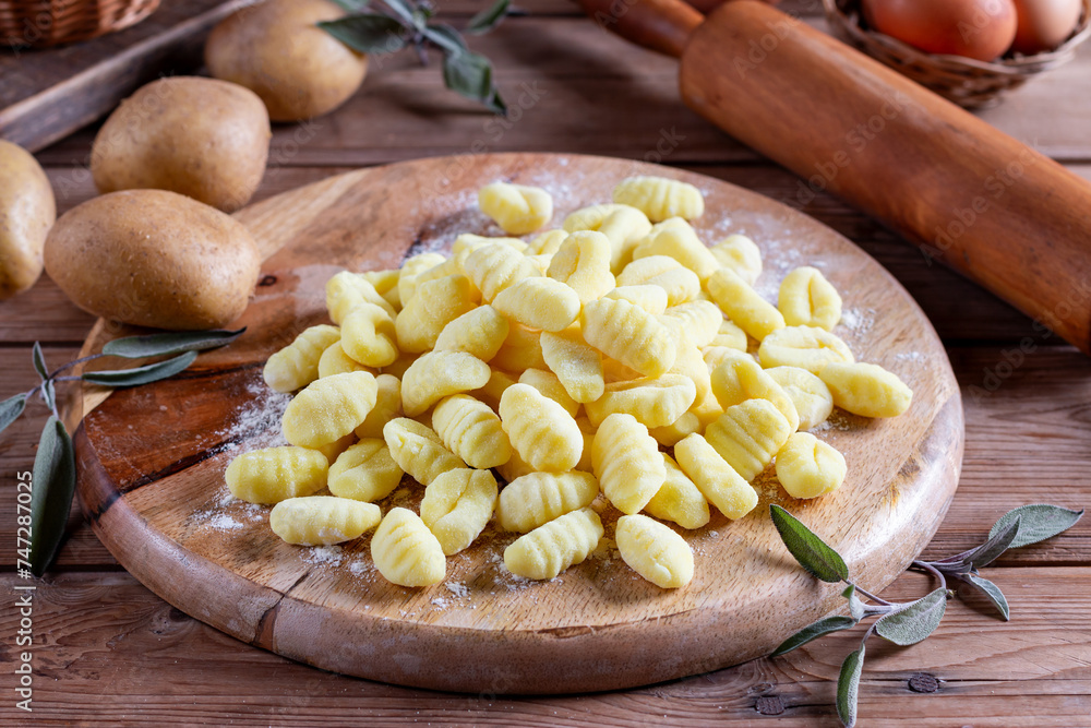 Fresh homemade uncooked gnocchi Italian dumplings on a floured wooden board in a kitchen with fresh greens behind in a close up Fresh homemade uncooked gnocchi Italian dumplings on a floured wooden board in a kitchen with fresh greens behind in a close up