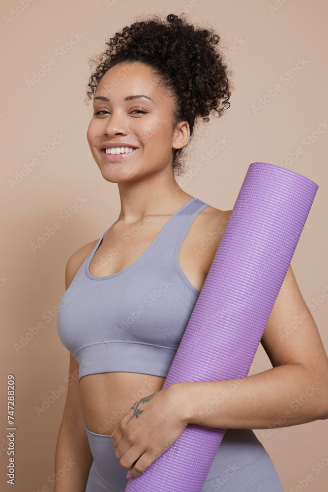 Studio portrait of smiling athletic woman with yoga mat