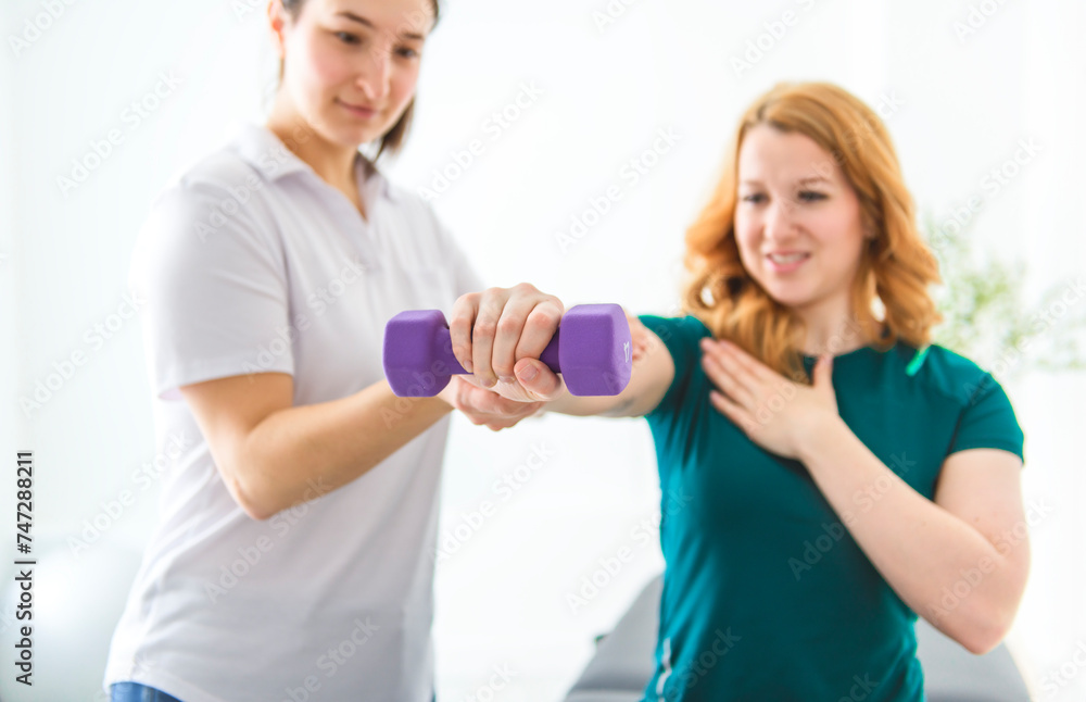 Modern rehabilitation physiotherapy at work with client holding dumbbell Modern rehabilitation physiotherapy at work with client holding dumbbell