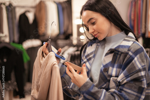 Shopping, clothes and style concept. Young brunette woman looking at price tag label in mall or clothing store.