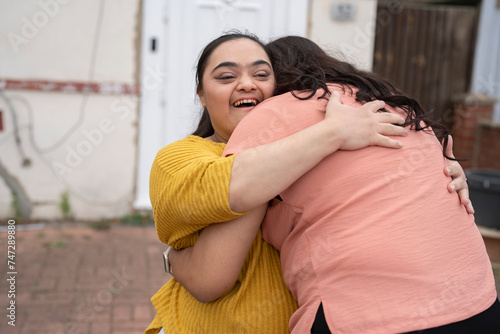 Woman embracing down syndrome daughter in front of house