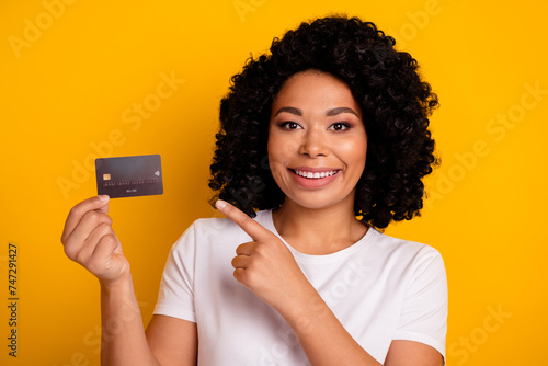 Photo of pleasant nice girlish woman with chevelure wear white t-shirt indicating at credit card isolated on yellow color background