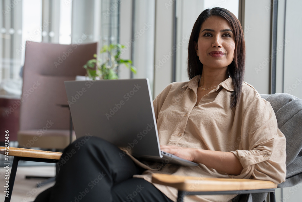 Businesswoman with laptop sitting in office lobby Businesswoman with laptop sitting in office lobby