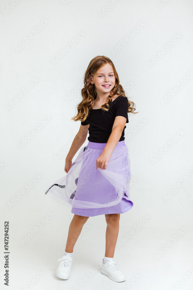 Smiling preteen girl in black t-shirt, violet skirt and white sneakers dancing and having fun on white background