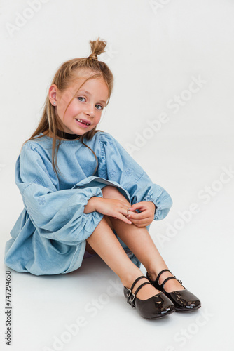 Little cute girl in beautiful blue dress is sitting on white background. Soft focus