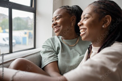 Portrait of happy lesbian couple looking through window at home