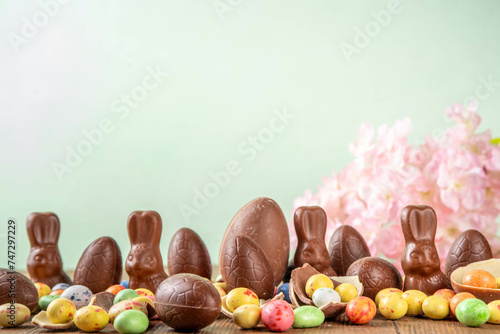 Easter background greeting card with holiday traditional confectionery, Easter egg hunt fun concept. Chocolate bunny, chocolate and candy Easter eggs on wooden background