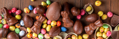 Easter background greeting card with holiday traditional confectionery, Easter egg hunt fun concept. Chocolate bunny, chocolate and candy Easter eggs on wooden background