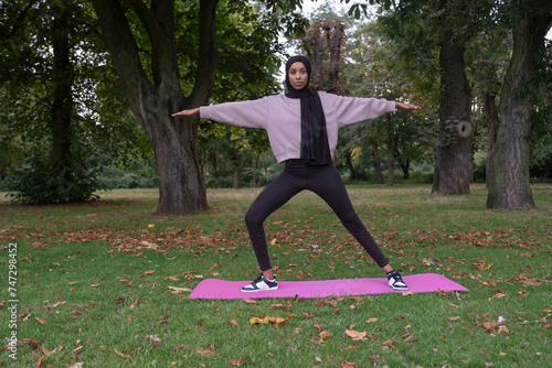 Portrait of woman in hijab in yoga warrior pose in park photo