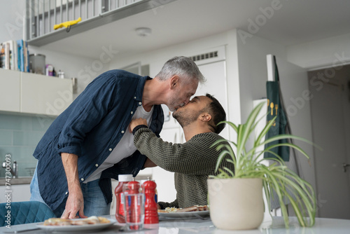 Male couple kissing and eating breakfast at home