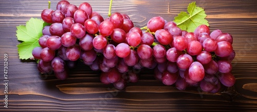 A cluster of red grapes sits on a wooden table, creating a simple yet vibrant display. The grapes appear fresh and ripe, ready to be enjoyed. photo