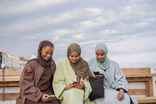 Three Muslin women using smart phones while sitting on bench