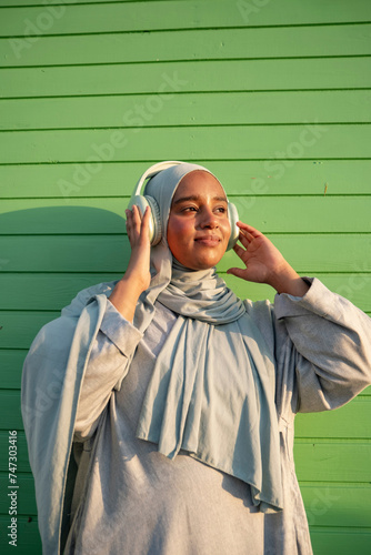 Portrait of Muslim woman listening to music against green wall