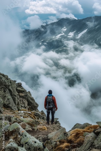 A lone hiker gazes into the valley from a fog-covered mountain summit, conveying reflection. Sports natural concept.