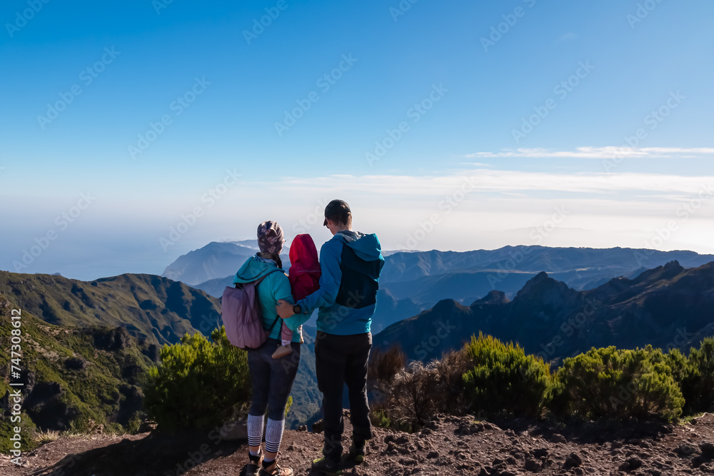 Hiker family with small child looking at scenic view of misty hills and canyon of rugged terrain on Madeira island, Portugal, Europe. Idyllic hiking trail to mountain peak Pico Ruivo. Aerial vista