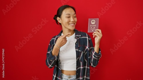 Cheerful young chinese woman parades her chinese passport, excitedly pointing with joy and confidence over a radically red isolated background! photo