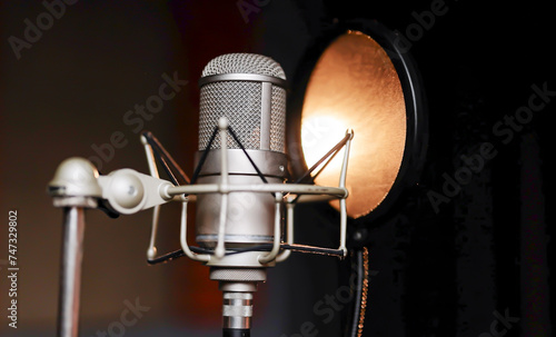 Close up studio condenser microphone with pop filter and anti-vibration mount live recording with colour lights background. Side view. Professional microphone close up in recording studio in light.