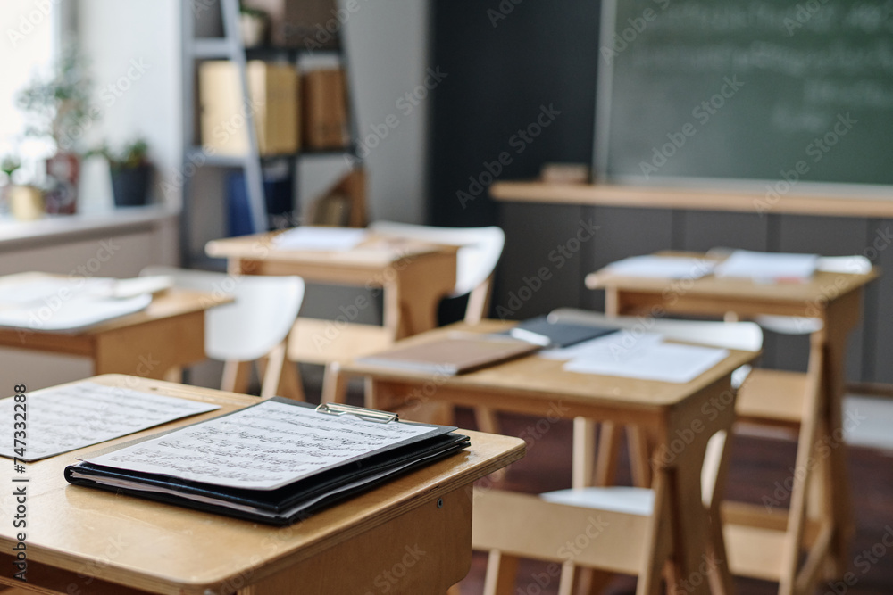 Selective focus no people shot of sheet music on wooden desk in modern classroom at school, copy space Selective focus no people shot of sheet music on wooden desk in modern classroom at school, copy space