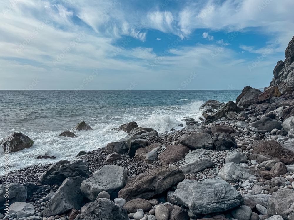 Scenic view of idyllic volcanic black stone beach Praia Garajai, Canico, Madeira island, Portugal, Europe. Sea waves smashing at shoreline of majestic Atlantic Ocean. Dramatic sky. Coastal landscape