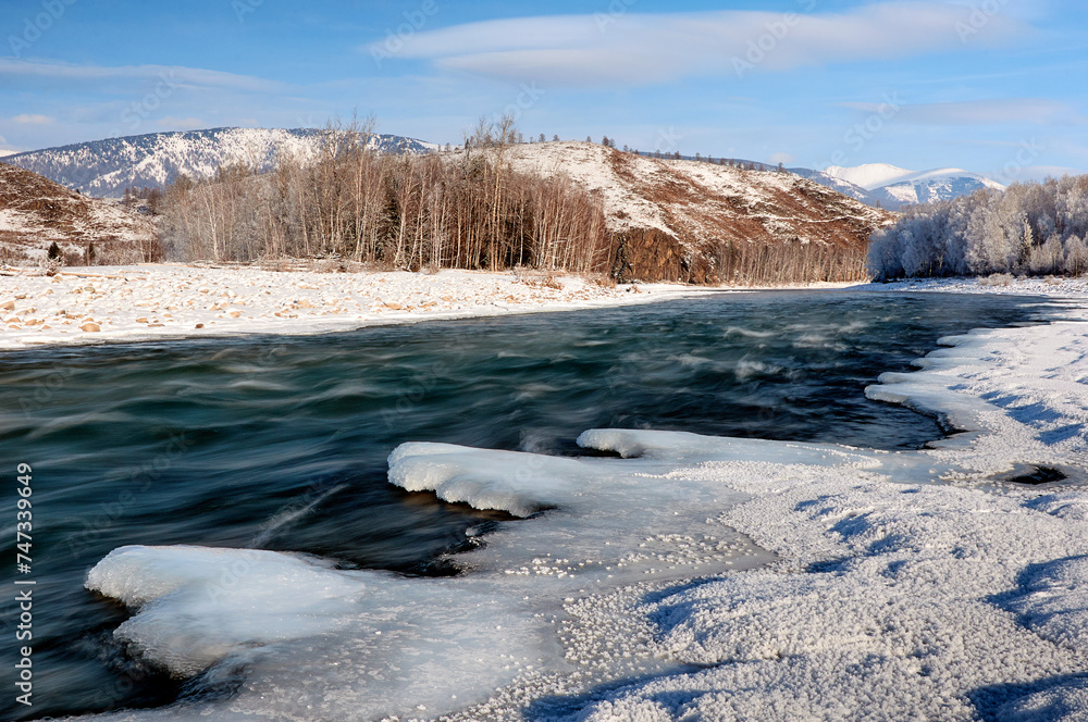 A frozen river bank with a distant mountain under a cloudy sky A frozen river bank with a distant mountain under a cloudy sky