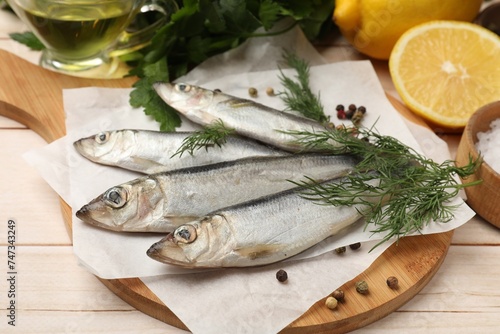 Fresh raw sprats, peppercorns and dill on light wooden table, closeup