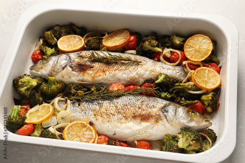 Delicious fish with vegetables and lemon in baking dish on light marble table