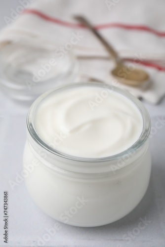 Delicious natural yogurt in glass jar on white table, closeup