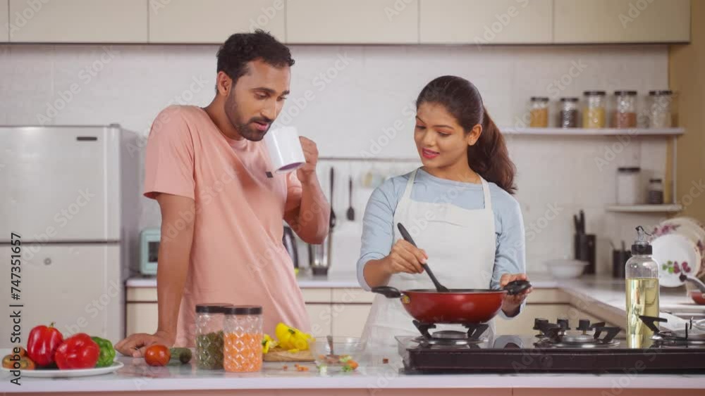 happy husband with coffee spending time with cooking wife at kitchen - concept of relationship bonding, morning routine and family affection. happy husband with coffee spending time with cooking wife at kitchen - concept of relationship bonding, morning routine and family affection.