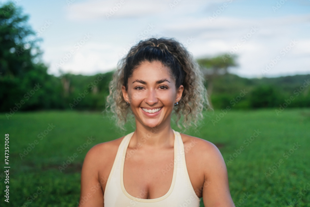 Portrait of a young attractive Latino athletic woman who does yoga against the backdrop of a green forest. Close-up of a yoga trainer, she looks at the camera and smiles. Wellness practice in nature. Portrait of a young attractive Latino athletic woman who does yoga against the backdrop of a green forest. Close-up of a yoga trainer, she looks at the camera and smiles. Wellness practice in nature.
