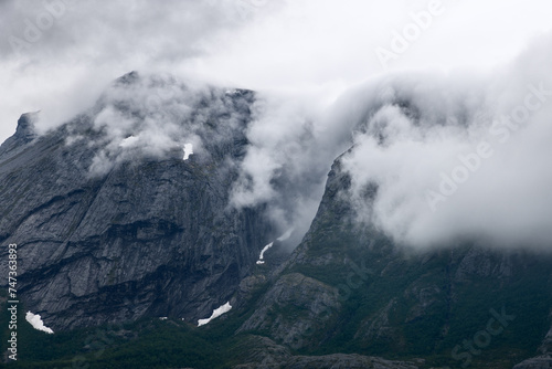 Billede på lærred Clouds cascade over the rugged cliffs of Norway, creating a dramatic interplay o