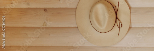 A light-colored straw beach hat hangs on the wooden wall, creating a summer vacation atmosphere. Concept for selling beach accessories or summer sales. Banner with copy space.