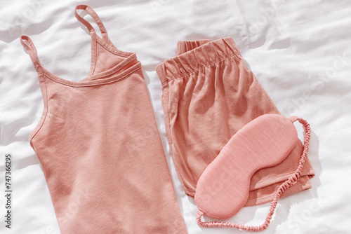 Top view pink pajama and eye sleep mask on white crumpled bedclothes. Cozy pyjamas for comfort rest at night. Flat lay from singlet, shorts, sleeping mask pastel pink color, sleep well photo