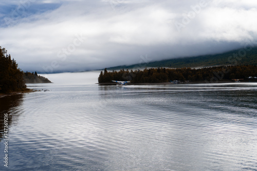 Fototapeta Naklejka Na Ścianę i Meble -  Port Alsworth, Alaska: Floatplane taking off on Hardenburg Bay on Lake Clark in Lake Clark National Park and Preserve. Inverted cloud layer, fog, Tanalian Mountain, seaplane, reflection.