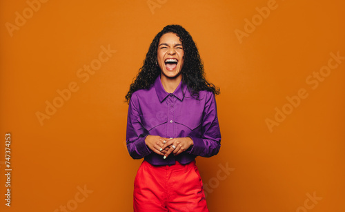 Vibrant woman in casual clothing on a colourful orange background laughing and smiling with joy