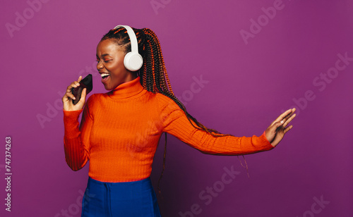 Happy girl singing and streaming music with headphones on purple background