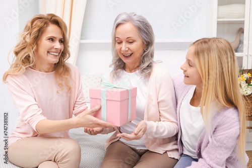 Smiling mother and teenage girl congratulate grandmother and give birthday present. Beautiful women generation