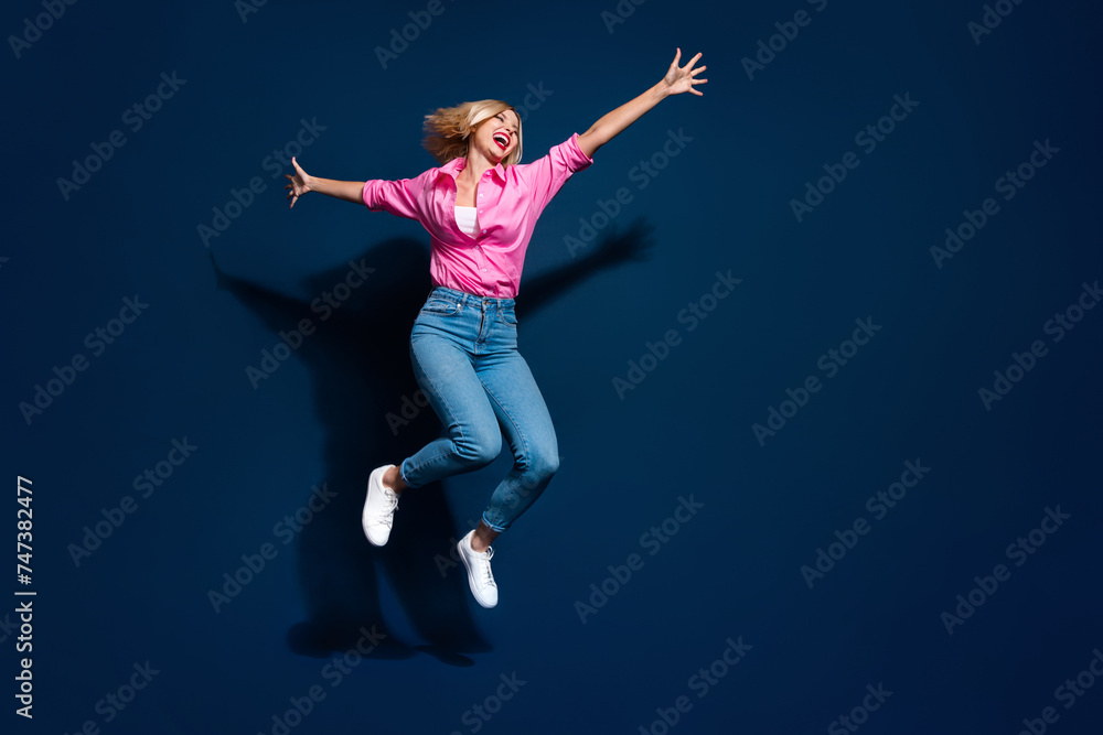 Full size photo of pretty young girl jumping have fun spread hands dressed stylish pink outfit isolated on dark blue color background