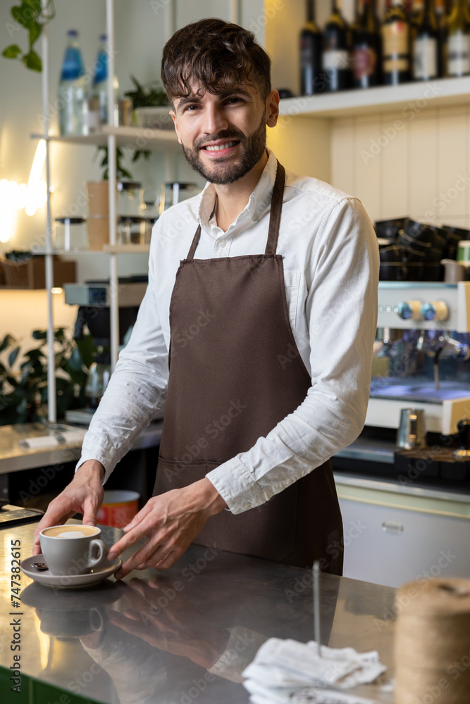 Man wearing apron holding coffee cup at cafe providing friendly service Man wearing apron holding coffee cup at cafe providing friendly service